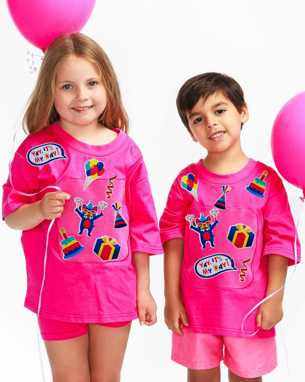 Boy and girl wearing pink TeeBoo™ Interactive Kids Gift Set with Yay, It's My Day! BooPatch™ pieces in organic cotton.
