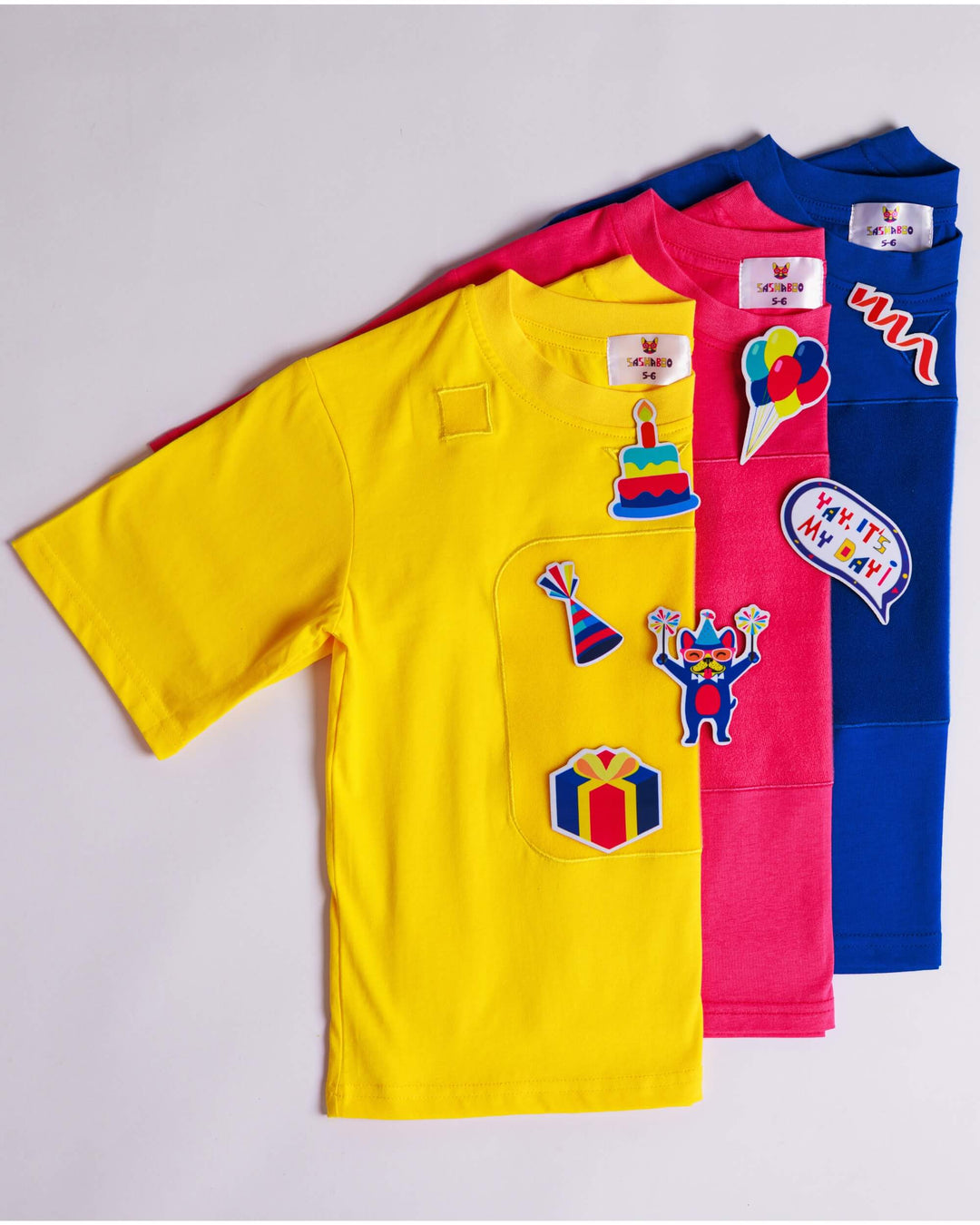 Yellow, pink and blue TeeBoo™ interactive organic cotton kids T-shirts with removable BooPatch™ Bithday gift-ready sets.