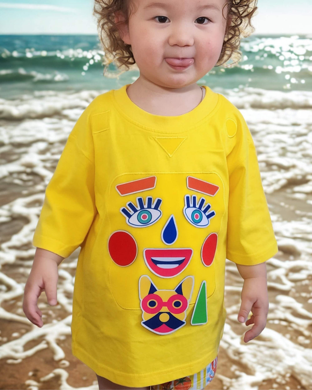 Child wearing a yellow TeeBoo™ interactive kids T-shirt with the Moody Friends BooPatch™ set at the beach.
