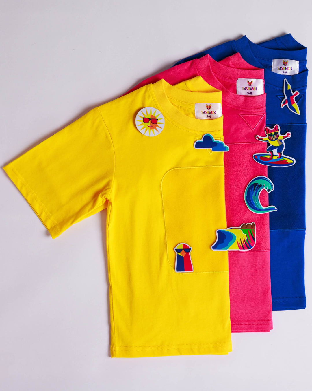 Yellow, blue and pink TeeBoo™ interactive organic cotton kids T-shirts with Sun.Fun.Surf. BooPatch™ gift sets.