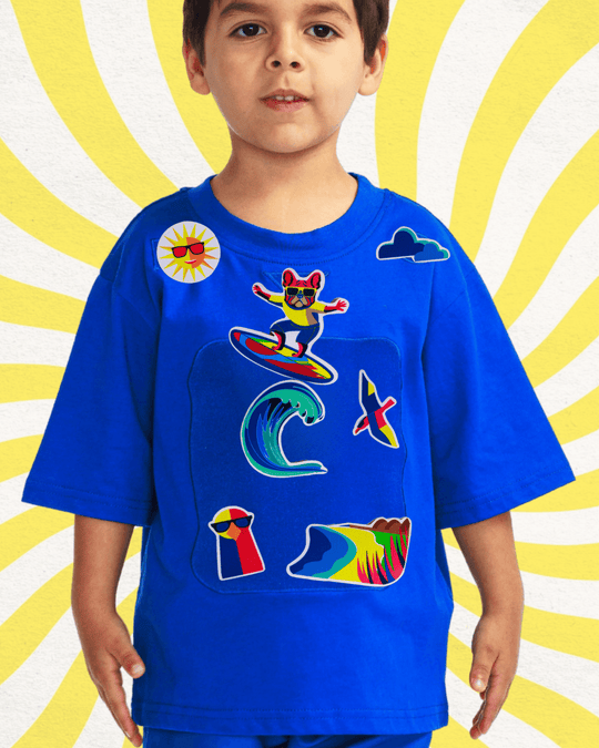 Child wearing a blue organic cotton TeeBoo™ interactive T-shirt with the Sun Fun Surf BooPatch™ set, featuring reusable surf-themed patches on a soft play panel for creative, screen-free fun.