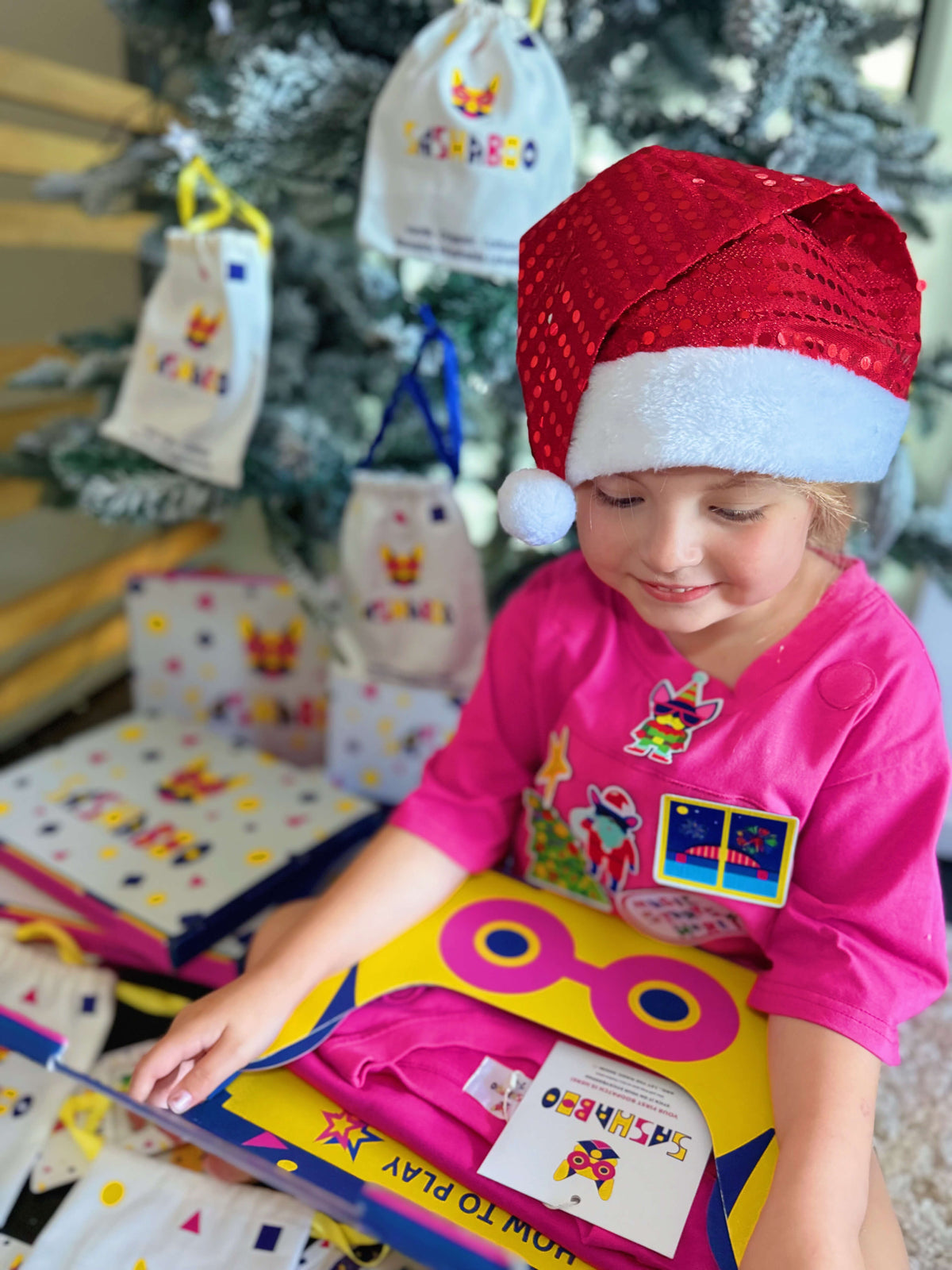 Child wearing a pink SASHABOO TeeBoo interactive kids T-shirt with festive BooPatch patches and a Santa hat, enjoying screen-free Christmas play.